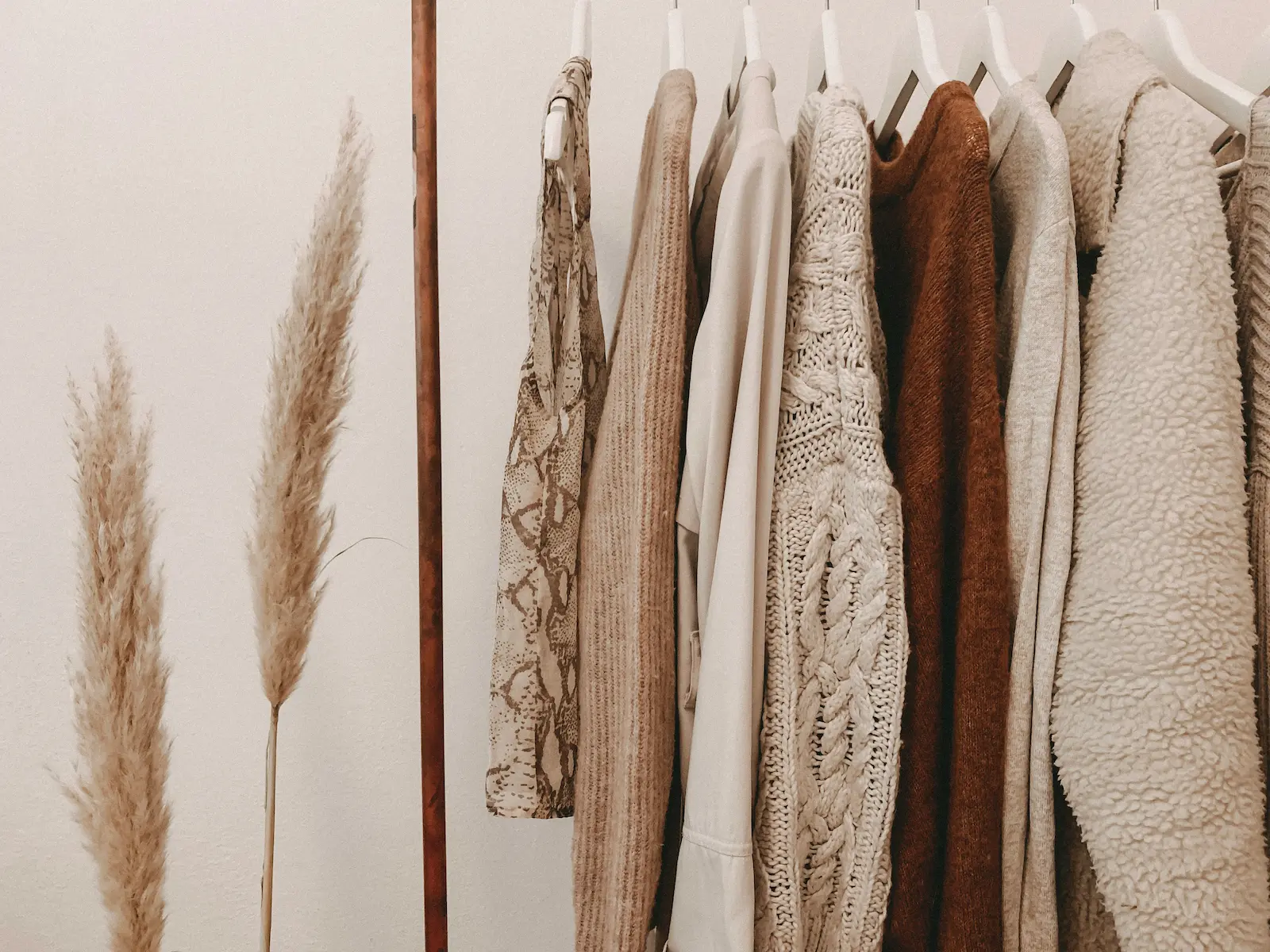 Neutral toned clothes hanging on a copper rail with dried pampas grass.